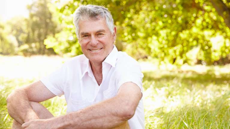 A smiling man sitting in the grass | dental implants Tamworth