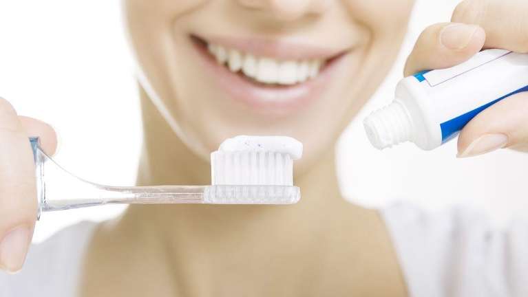 A smiling woman putting toothpaste on her toothbrush | fluoride Tamsworth